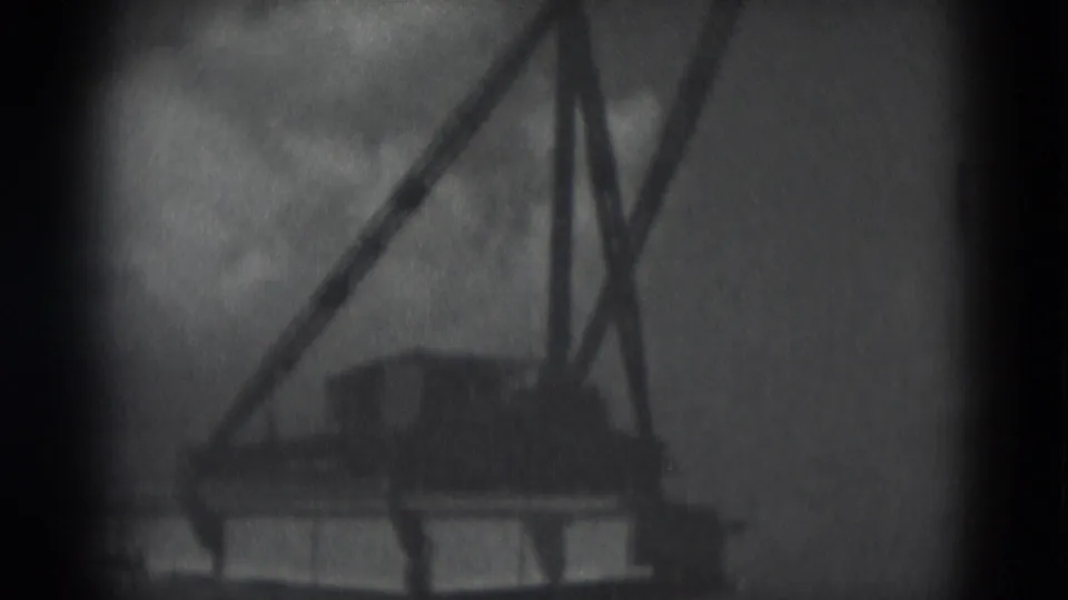 Close-up 8mm frame from the bridge construction sequence showing crane rigging silhouetted against clouds.