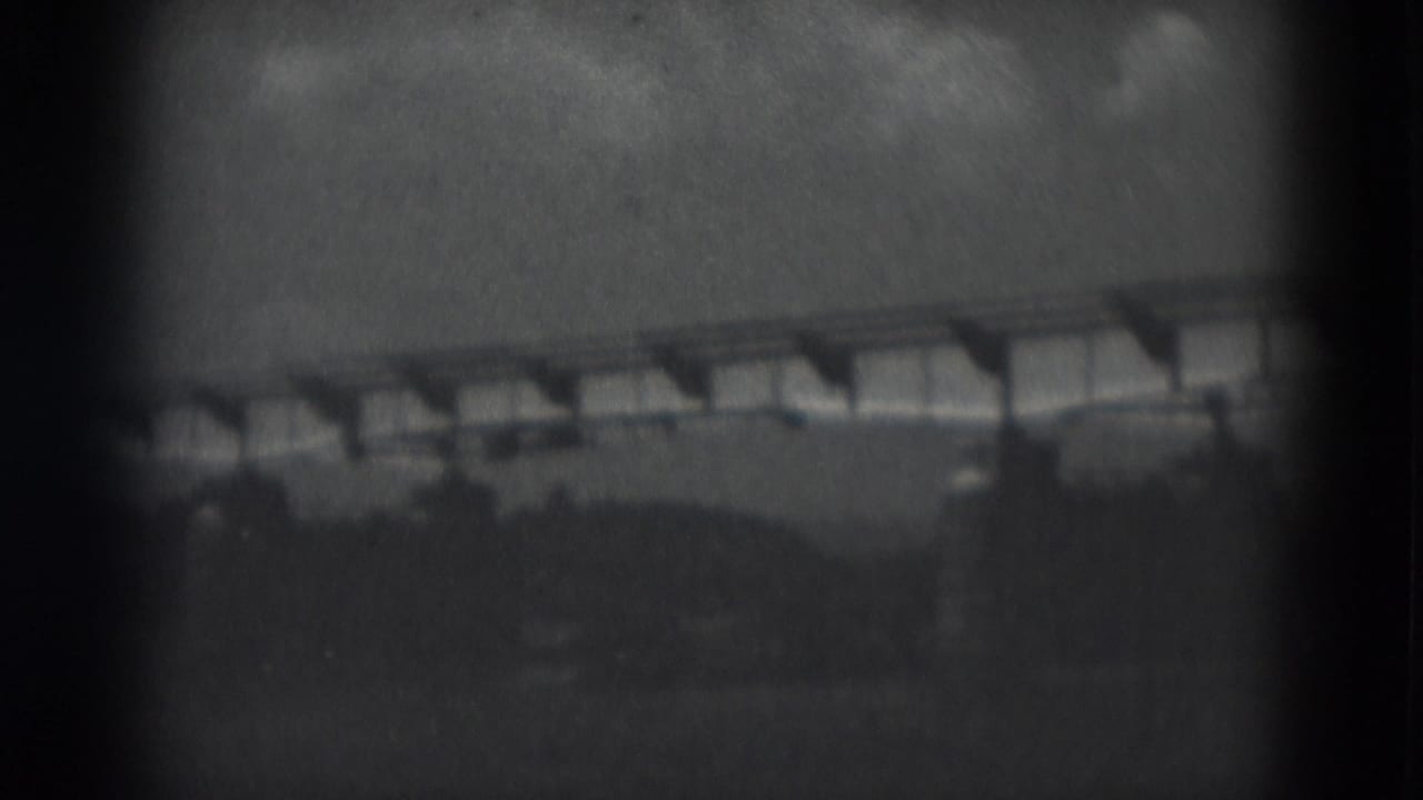 1975 8mm frame from Middletown, Pennsylvania showing a distant low bridge or elevated structure beyond open land.
