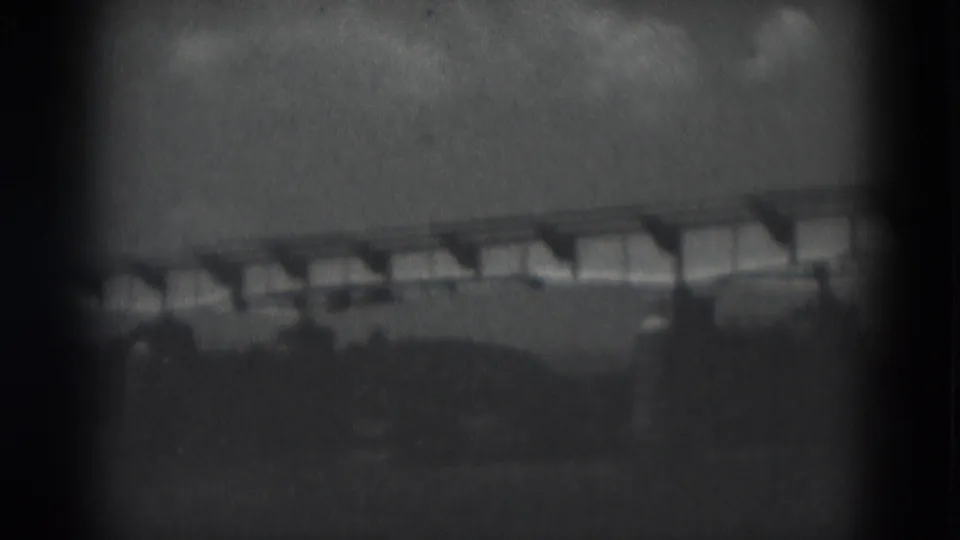 1975 8mm frame from Middletown, Pennsylvania showing a distant low bridge or elevated structure beyond open land.