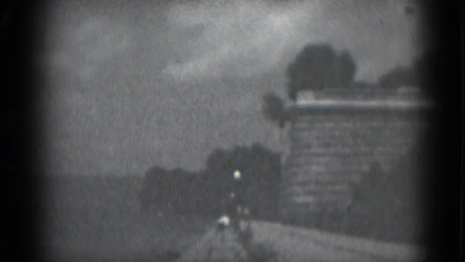 Grainy 1975 Middletown, Pennsylvania frame showing a stone wall or roadside barrier with trees and open land beyond.