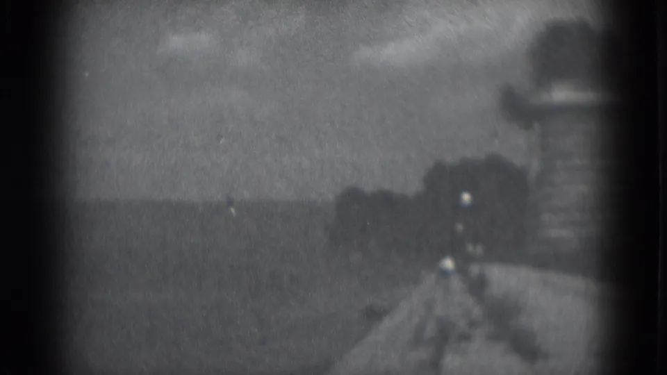 Grainy 1975 8mm frame showing a blurred waterfront approach in Middletown, with dark water, a gray sky, and indistinct shoreline.
