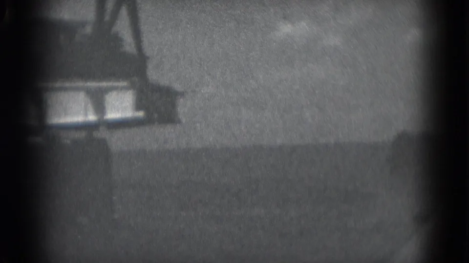 Final 8mm frame shows part of a waterfront structure or dock detail above dark water, with heavy grain and a gray sky.