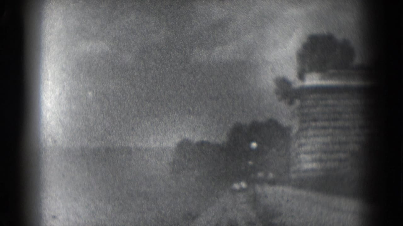 Soft black-and-white frame with a distant outdoor scene partly obscured by dark film edges.
