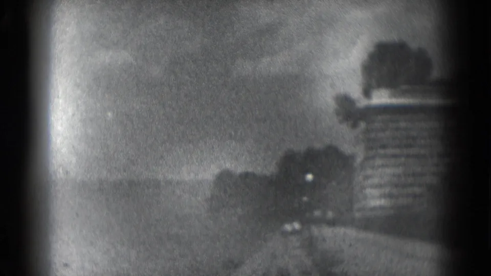 Grainy 8mm opening frame from the Middletown reel, showing a distant outdoor scene through heavy dark framing and soft exposure.