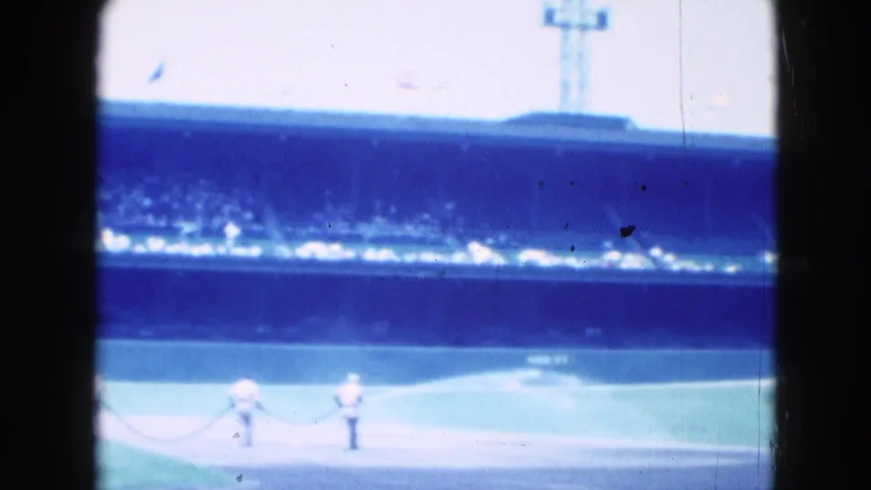 Wide 8mm view of the Middletown baseball stadium, with the field below a crowded stand and small figures near a rope line.