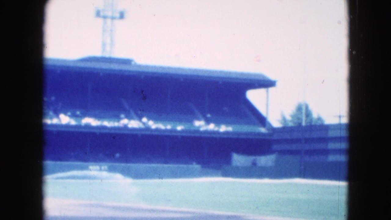 1975 8mm view in Middletown, Pennsylvania showing a baseball field edge, covered grandstand, and tall light tower.