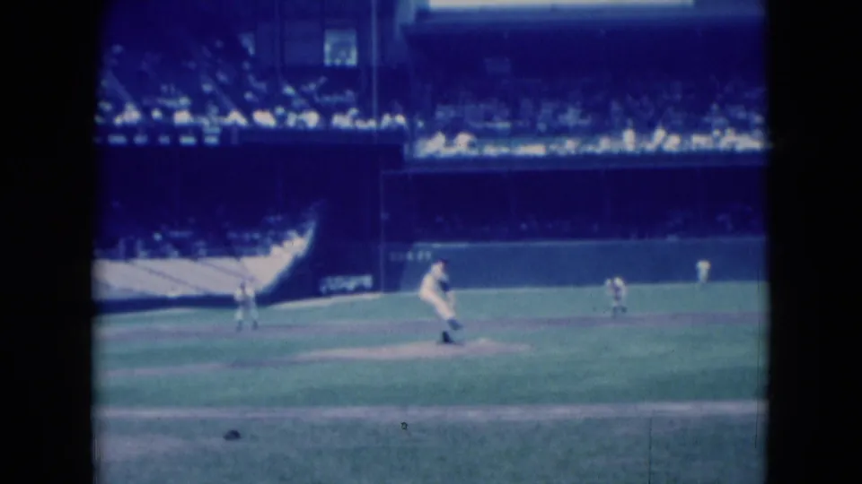 1975 Middletown baseball game view with a pitcher on the mound, fielders in position, spectators in the grandstand, and soft 8mm color.