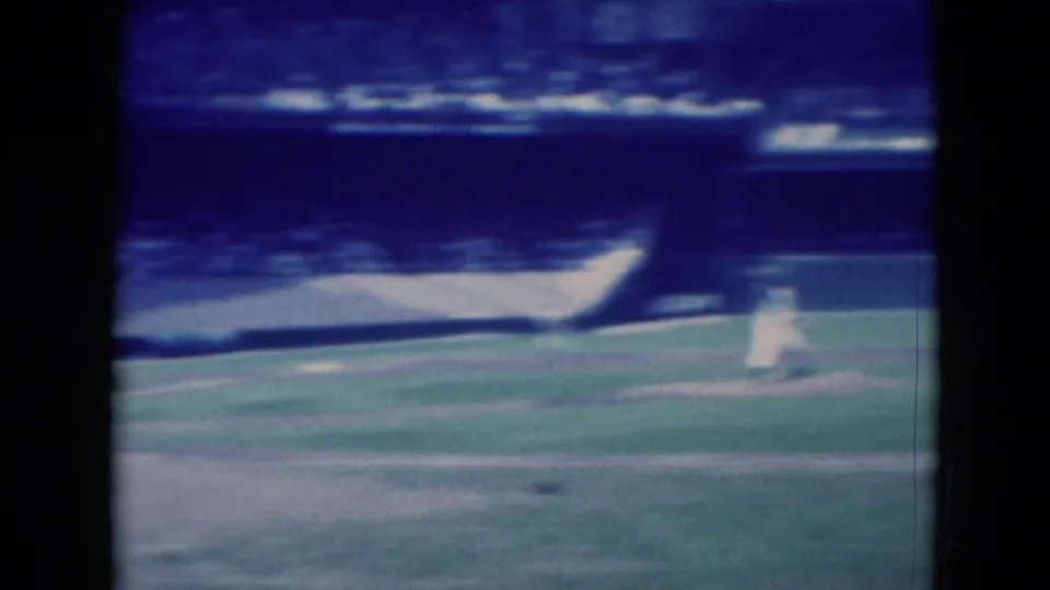 The pitcher appears in motion during the 1975 Middletown baseball game, filmed from a distant spectator viewpoint on 8mm.