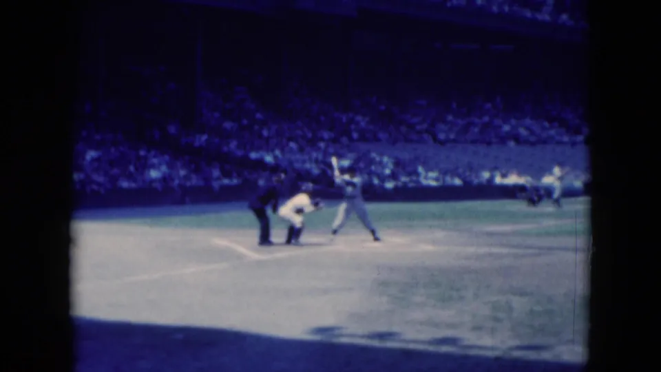 A batter stands at home plate during the Middletown baseball game, with nearby officials or catcher and a shaded crowd behind him.