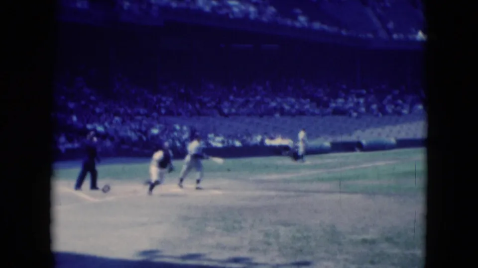 1975 8mm baseball footage from Middletown showing movement around home plate after a hit, with stands in the background.