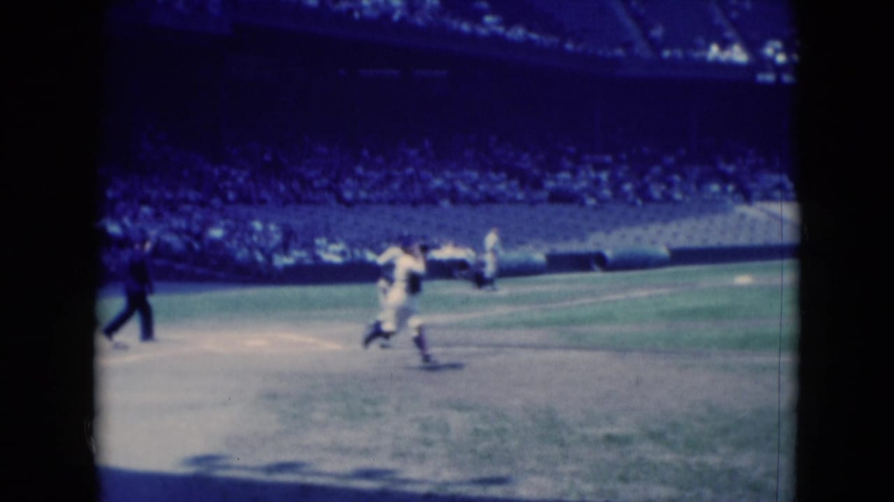 1975 8mm frame from Middletown, Pennsylvania, showing a baseball player running near the infield with teammates and spectators in the background.