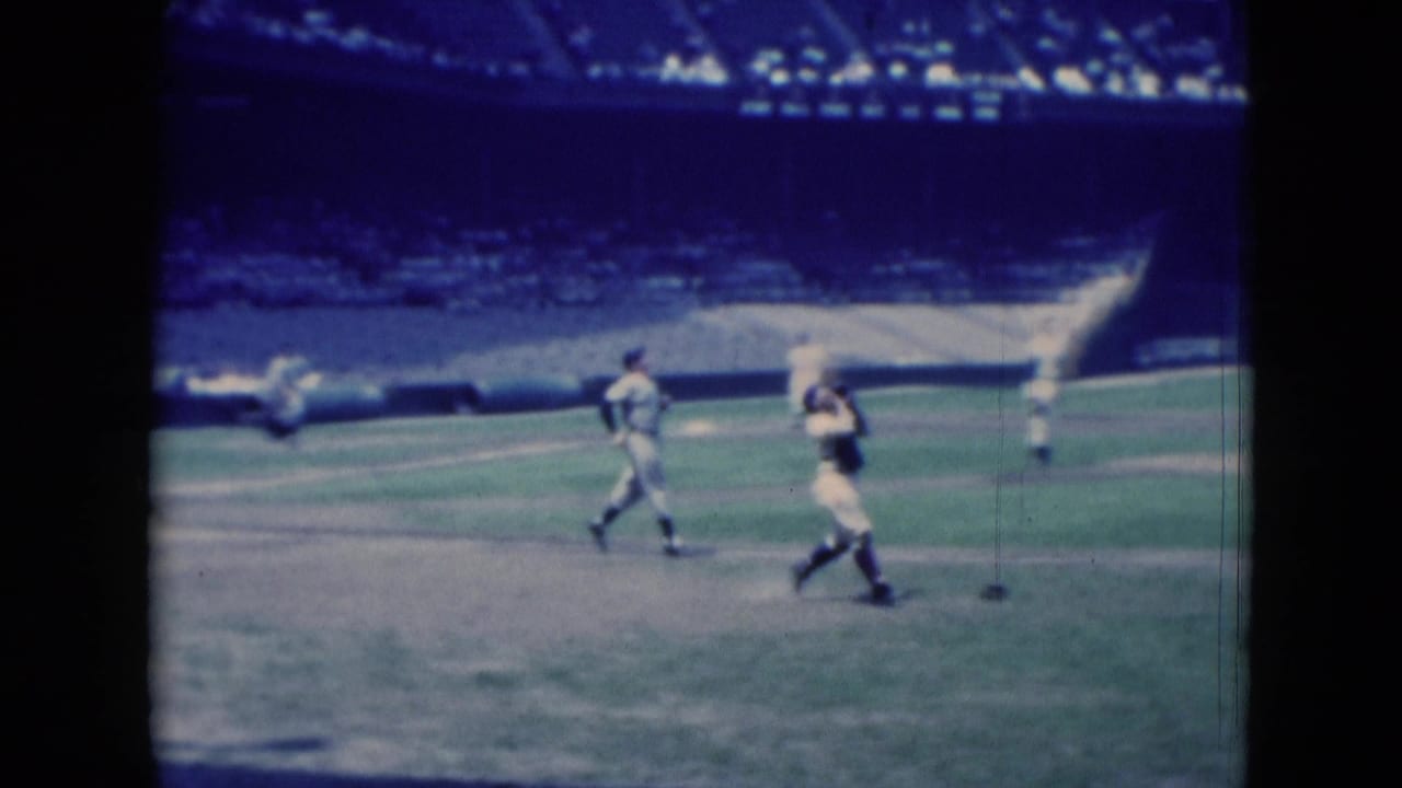 Two baseball players move across the field with empty seats and spectators in the stadium behind them.
