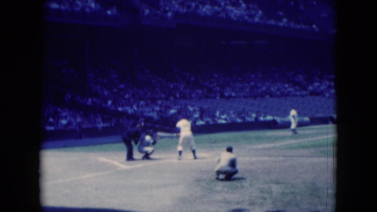 Pitcher prepares on the mound as batter, catcher, and umpire wait at home plate.