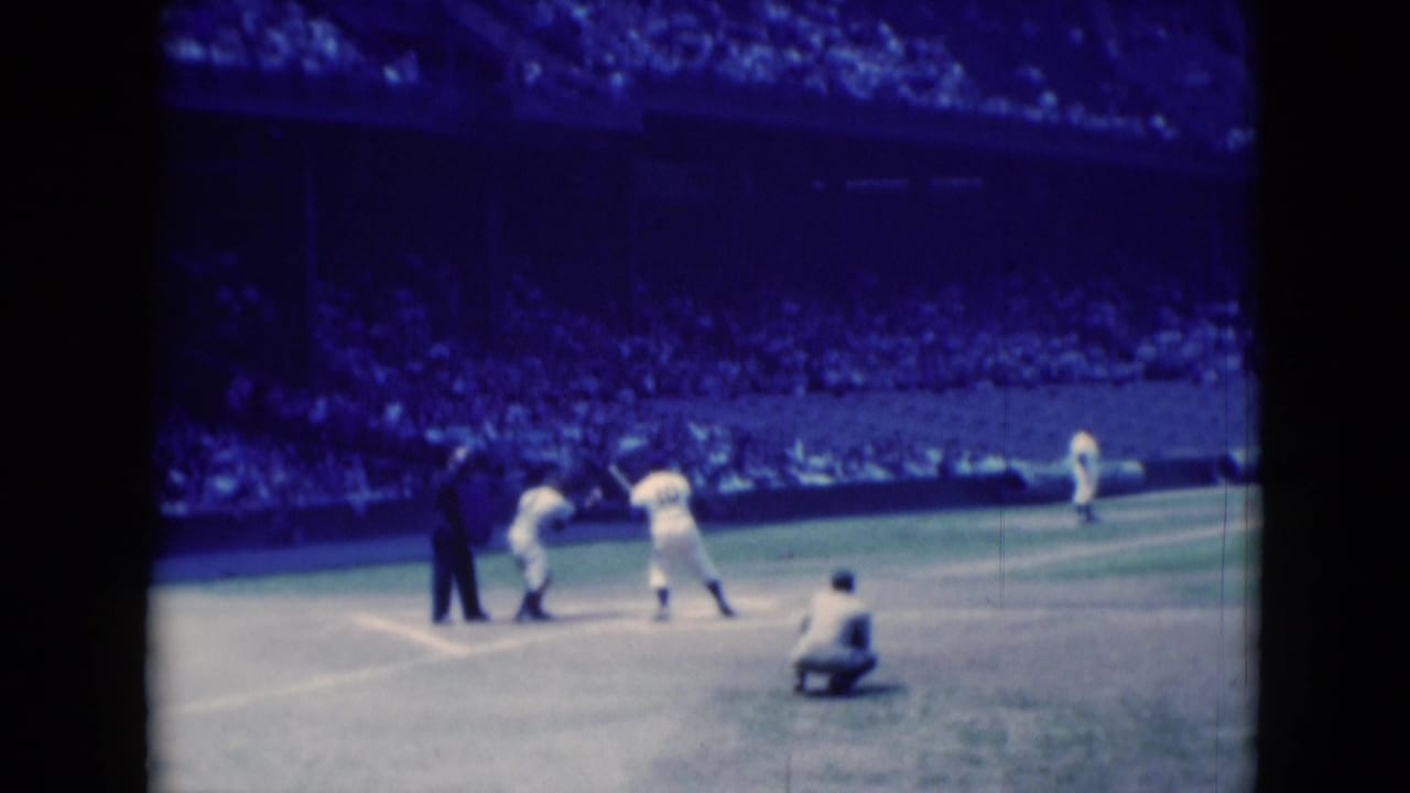 The batter swings at a pitch in the 1975 Middletown baseball scene, with catcher, umpire, pitcher, and spectators visible.