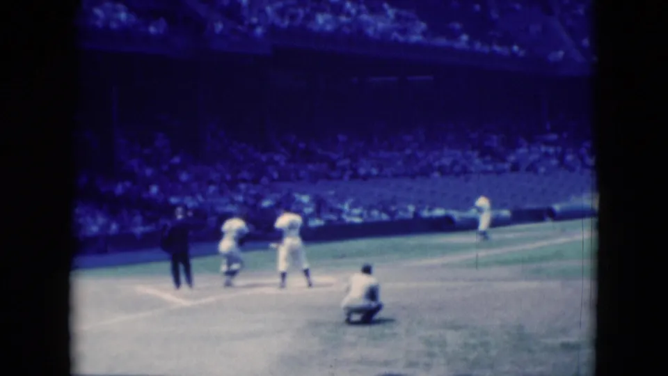 The 1975 Middletown baseball footage shows players near home plate after the pitch, with umpire, catcher, pitcher, and packed stands visible.