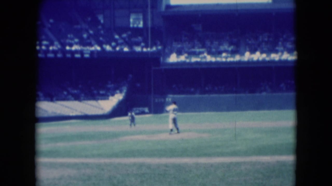 Distant baseball players on a field with stadium seats and an outfield wall behind them.