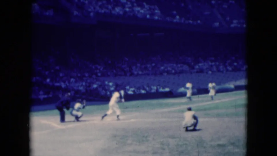Home plate action in the 1975 Middletown baseball footage, with a batter, catcher or umpire, fielders, and spectators in the background.
