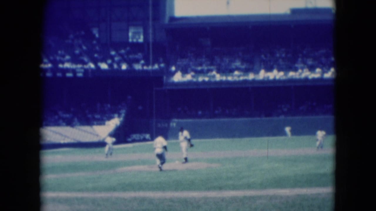 1975 8mm home-movie frame from Middletown, Pennsylvania, showing baseball players on the field with crowded stadium seating in the background.
