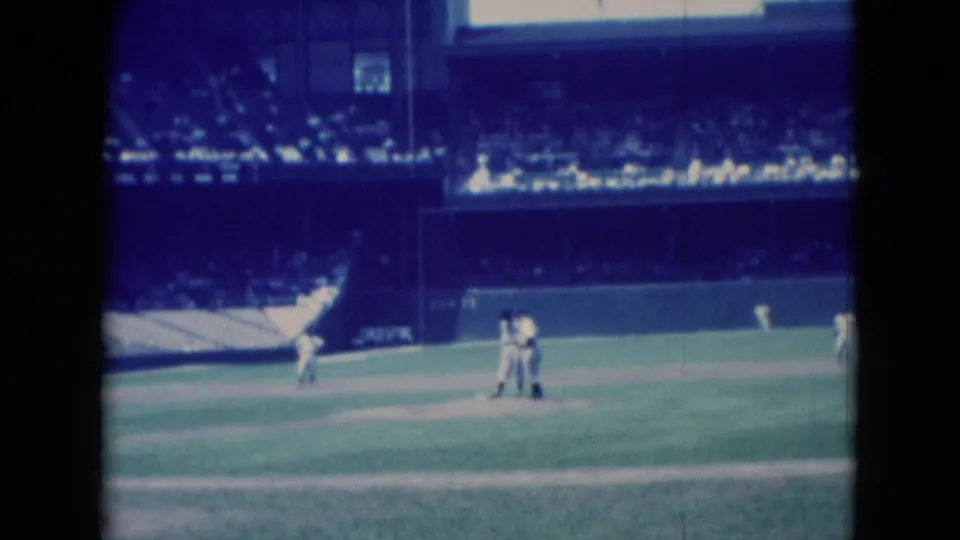 1975 8mm frame from Middletown, Pennsylvania, with several baseball players on the field and distant spectators in the stadium stands.