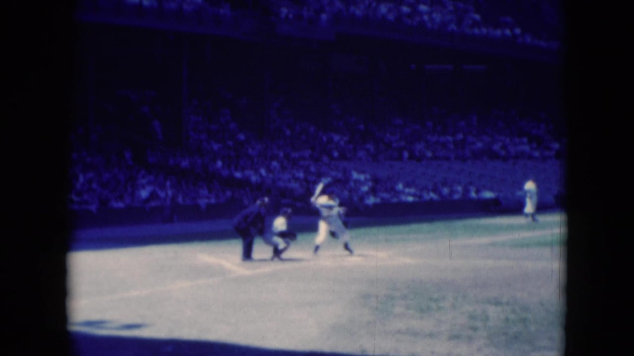 Batter swings at home plate as catcher and umpire watch on a sunlit baseball field.