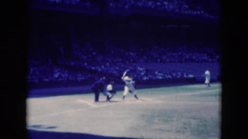 Middletown, Pennsylvania 1975 8mm frame showing a batter swinging near home plate with catcher, umpire, fielders, and crowd visible.