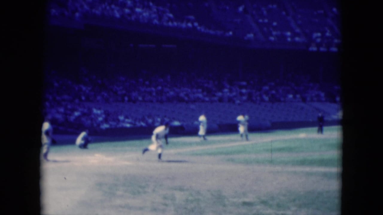 Middletown, Pennsylvania 1975 frame showing players shifting after the hit, with the catcher near home plate and a large crowd in the background.
