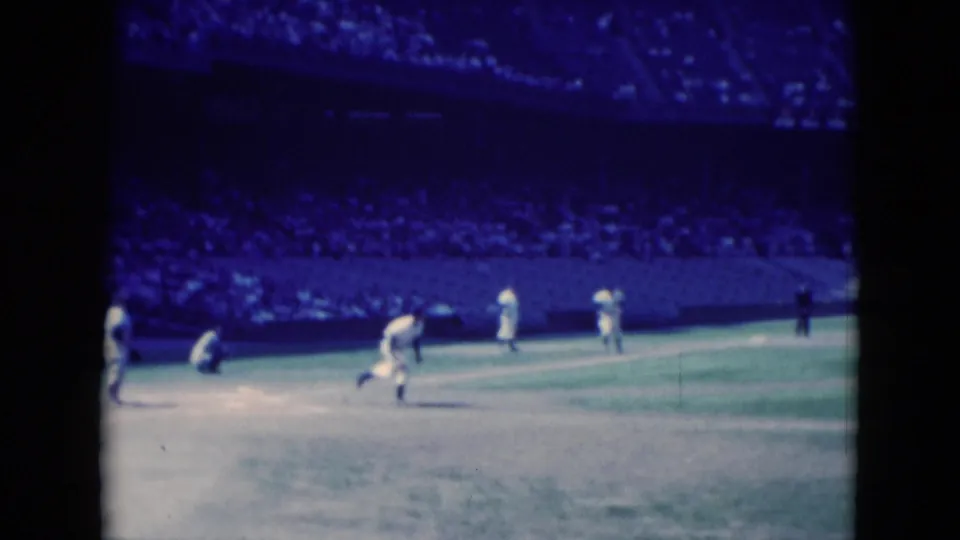 Middletown, Pennsylvania 1975 frame showing players shifting after the hit, with the catcher near home plate and a large crowd in the background.