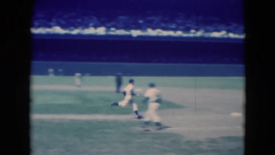 Middletown, Pennsylvania 1975 frame showing a runner moving toward first base as a fielder waits near the baseline on the sunlit infield.