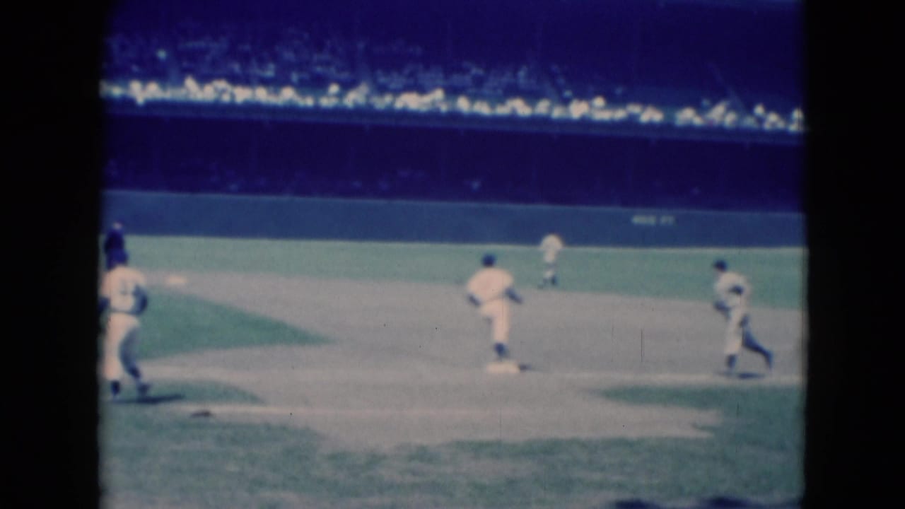 Baseball players move across an infield with stadium seating in the background.