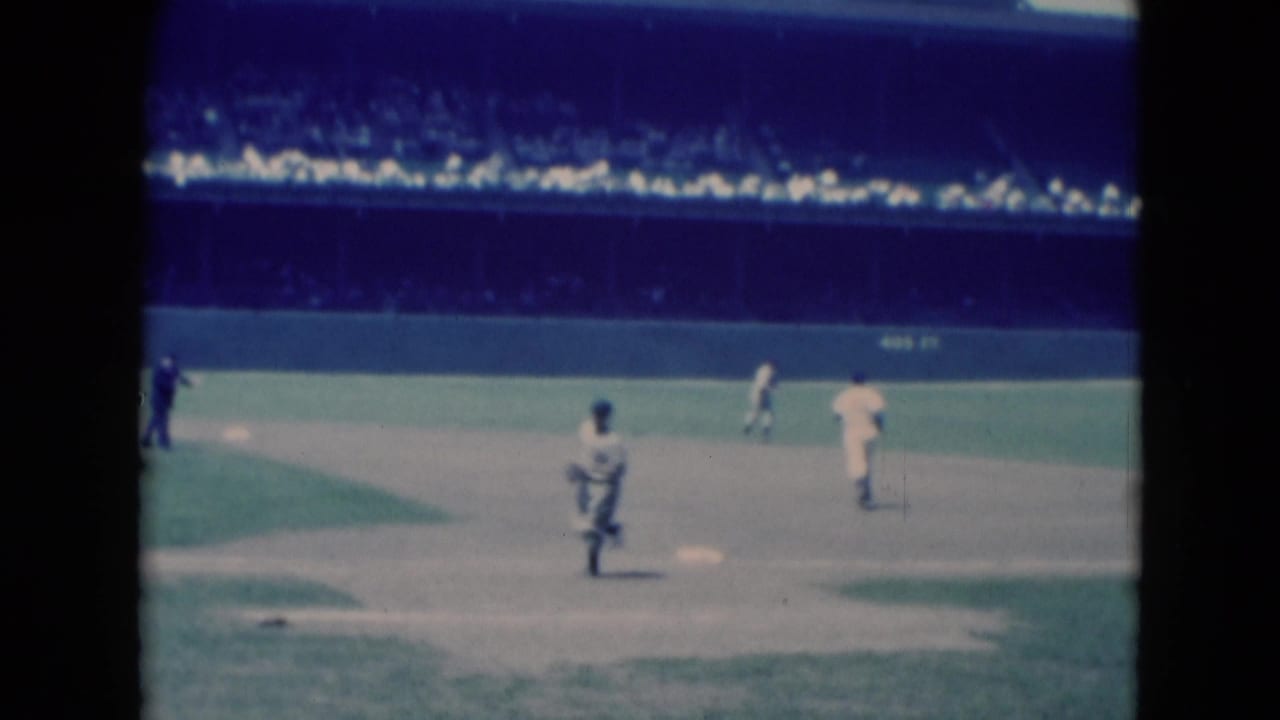1975 Middletown, Pennsylvania 8mm frame with players near the infield and a dark-clad official against a stadium crowd.