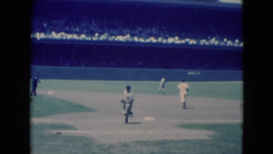 1975 Middletown, Pennsylvania 8mm frame with players near the infield and a dark-clad official against a stadium crowd.