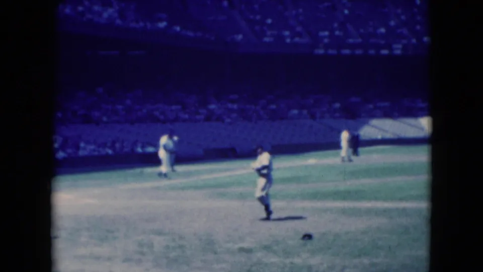 1975 Middletown, Pennsylvania 8mm frame showing a foreground player on the field with teammates near the bases and spectators beyond.