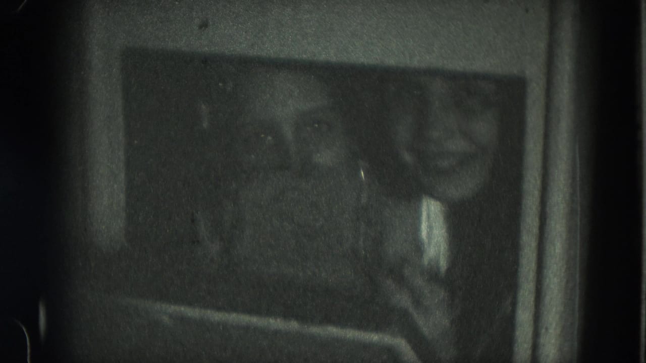 In a dark 8mm interior, two girls look toward the camera with one face clearer and the other receding into shadow.