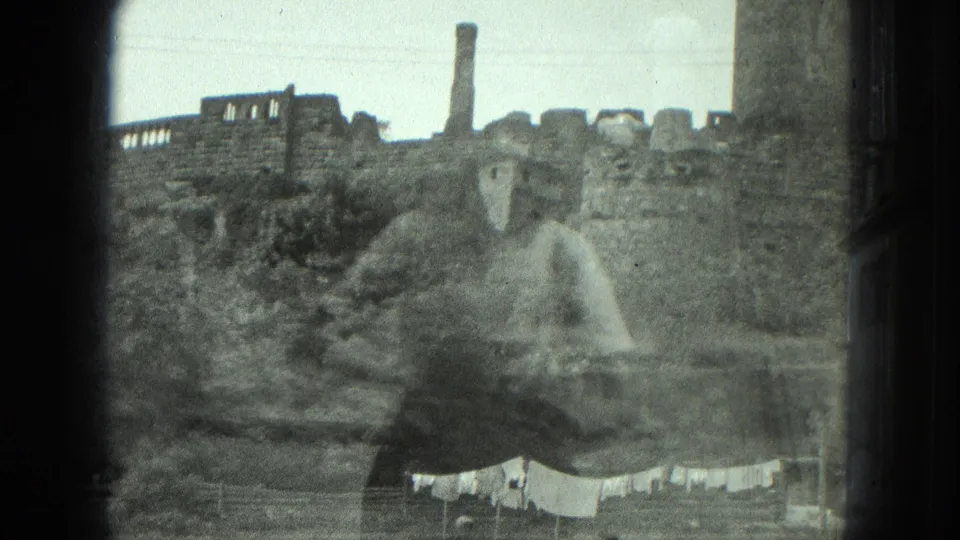 A grainy 1975 8mm frame listed as Milwaukee shows the ruin closer, with a chimney above the wall and laundry below.