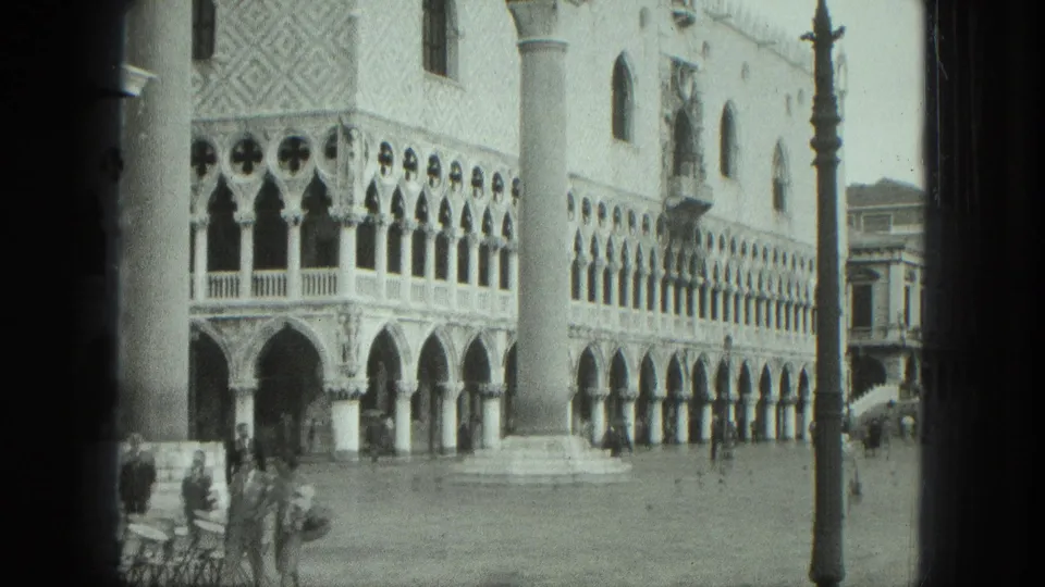 1975 Venice view of the Doge's Palace arcades, a tall piazza column, cafe seating, and pedestrians in the square.
