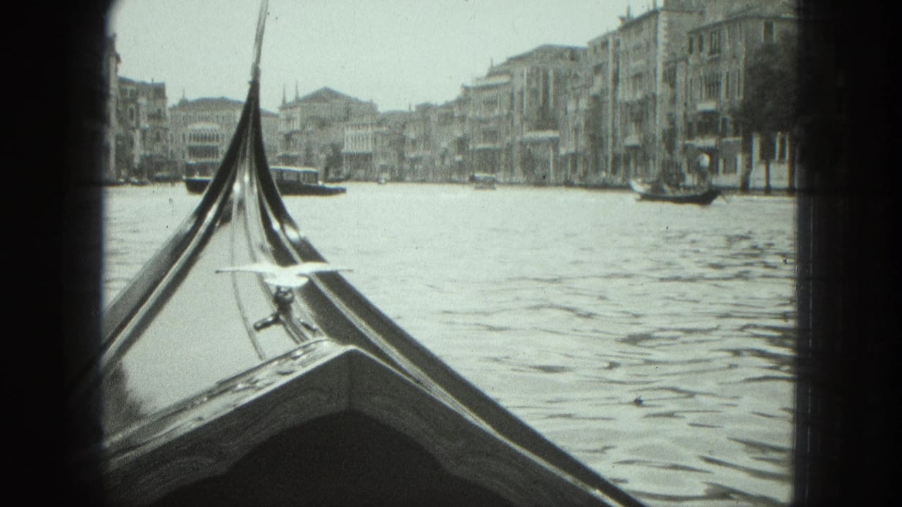 1975 Venice 8mm frame looking over a gondola bow across canal water toward historic waterfront buildings.