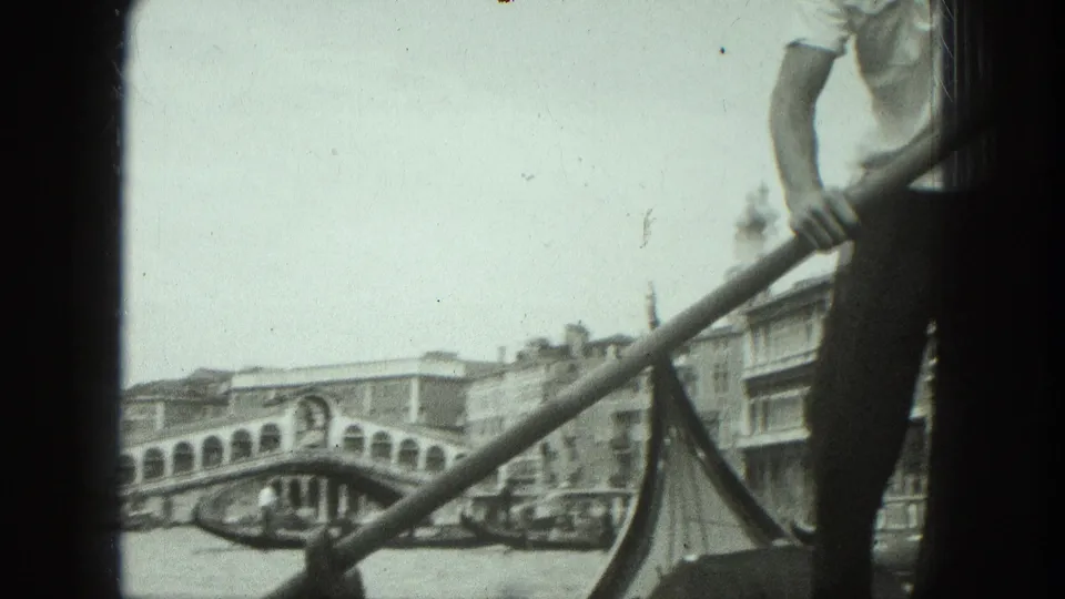 1975 Venice canal frame with a partly visible gondolier rowing near the Rialto Bridge, seen from a low boat-level angle.