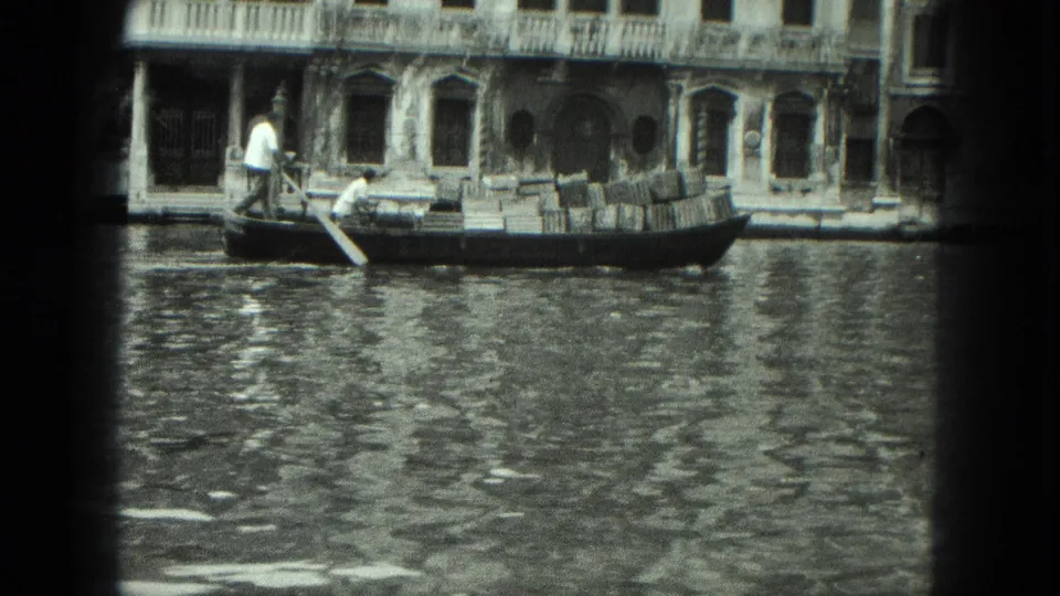 1975 Venice 8mm frame showing a gondolier guiding a loaded gondola past weathered canal-front facades.