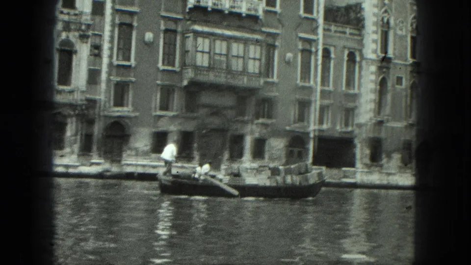 1975 Venice home-movie frame showing the gondola farther along the canal beneath balconies and arched openings.