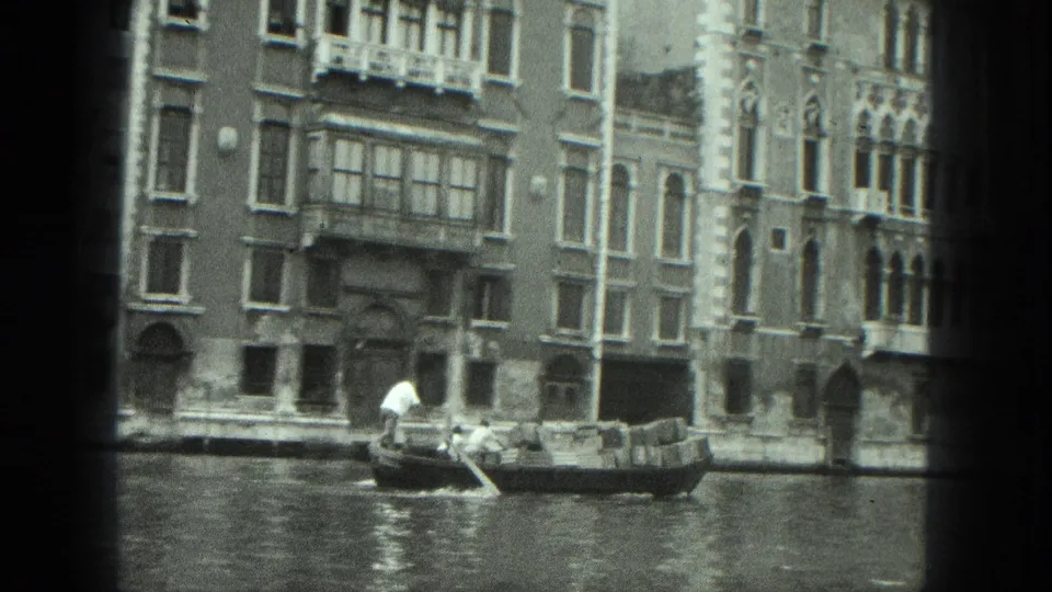 1975 Venice home-movie frame showing a gondola and gondolier on a canal before ornate waterfront architecture.