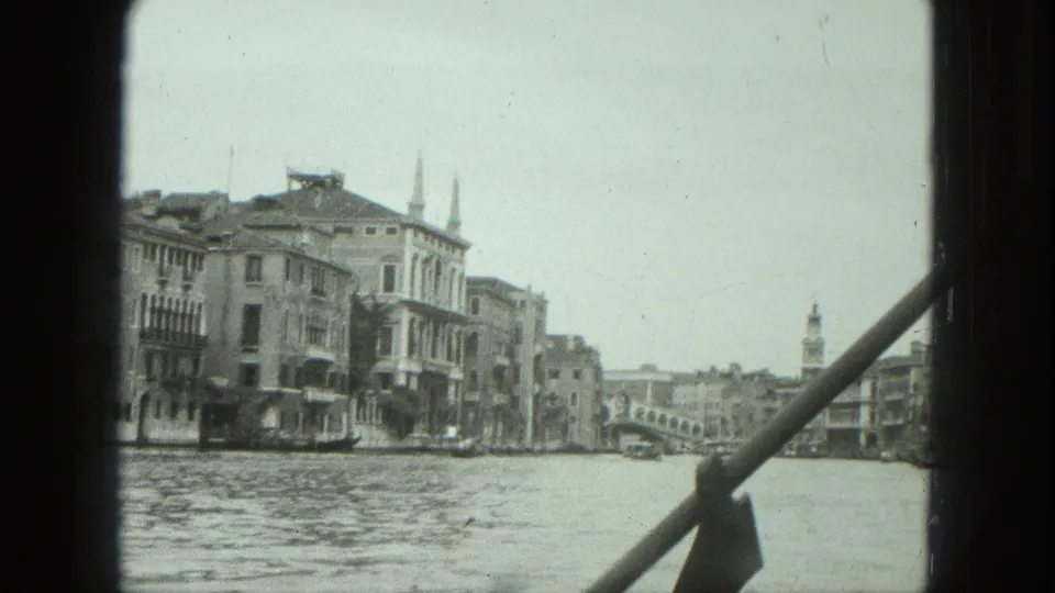 1975 Venice home-movie view across a canal toward buildings, small boats, a bridge, and distant tower forms.
