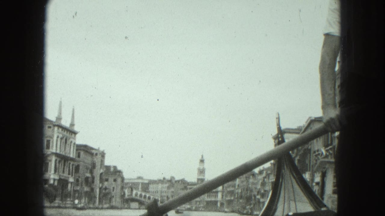 Gondola prow and rowing pole frame a canal lined with historic buildings and a distant tower.
