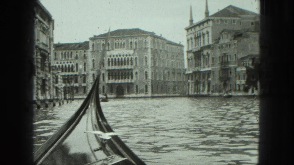 1975 8mm Venice canal view from a gondola, with rippling water and historic arched facades ahead.