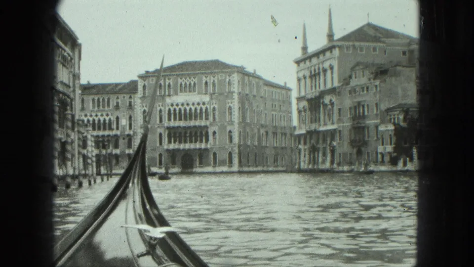 1975 Venice home-movie frame showing a gondola bow, canal reflections, and multi-story historic facades.