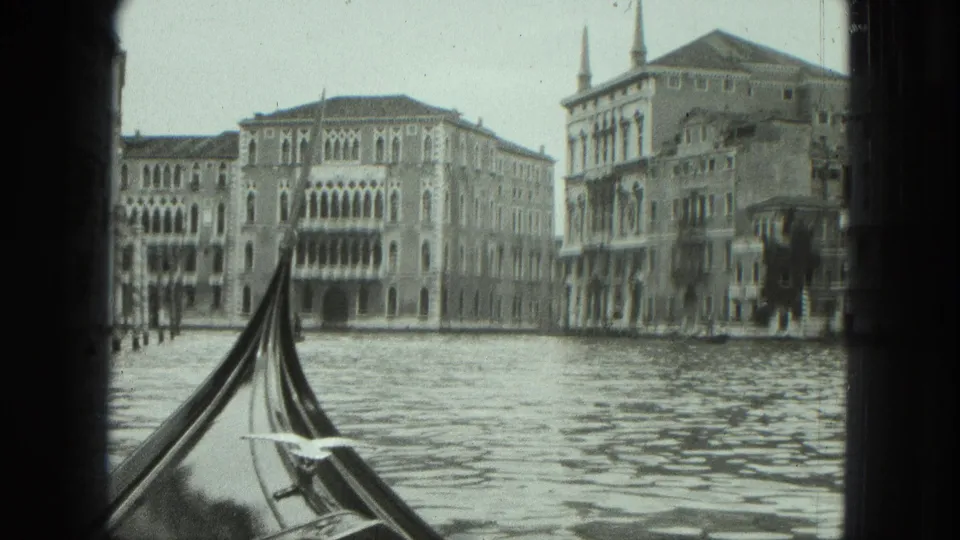 1975 8mm view from a gondola in Venice, with historic facades across the canal and textured water in front.