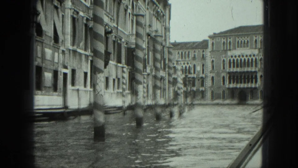 1975 Venice canal footage from a moving gondola, looking past waterside walls toward arched buildings ahead.
