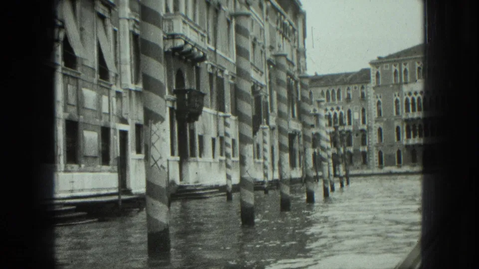1975 Venice boat-level view of a canal, with striped poles, waterfront facades, and soft 8mm framing from inside or beside the gondola.