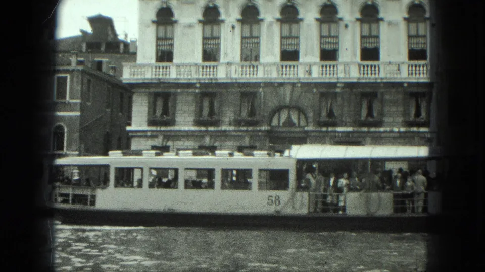 1975 8mm Venice frame showing a public water bus marked 58 with passengers beside palazzo-style canal facades.