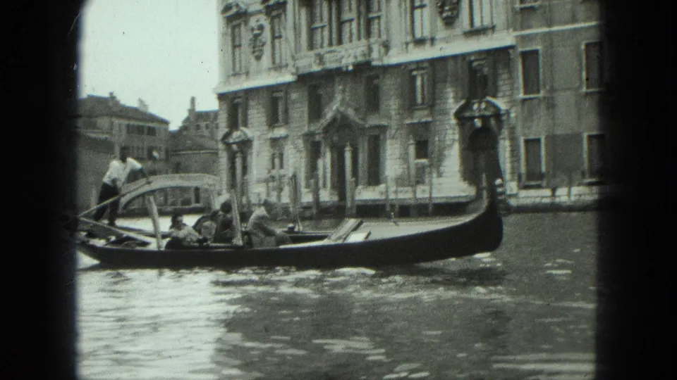 1975 Venice home-movie frame of a gondola carrying passengers along a canal beside ornate waterfront architecture.