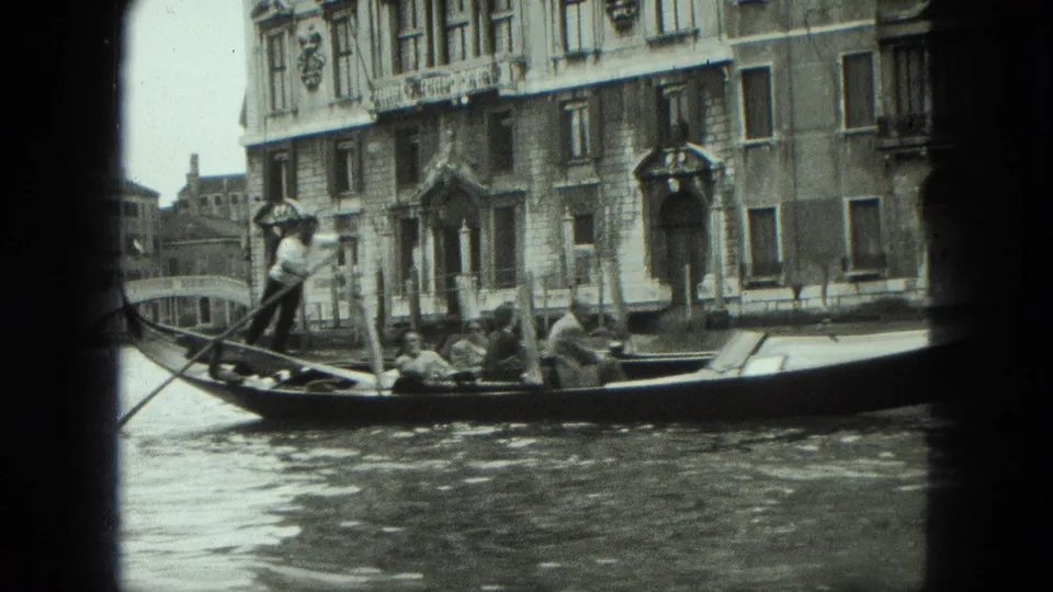 1975 Venice canal shot with a gondola in the foreground, a gondolier rowing, and historic building facades behind.